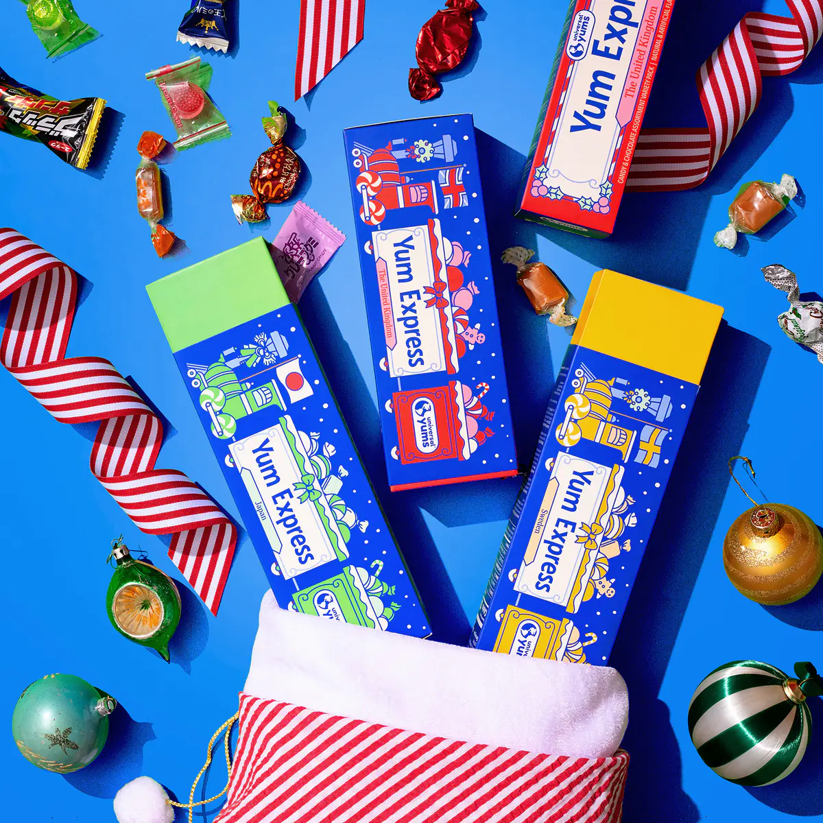 Yum Express candy boxes from Japan, the United Kingdom, and Sweden spilling out of a striped holiday stocking, with candies, ribbons, and ornaments on a blue background.
