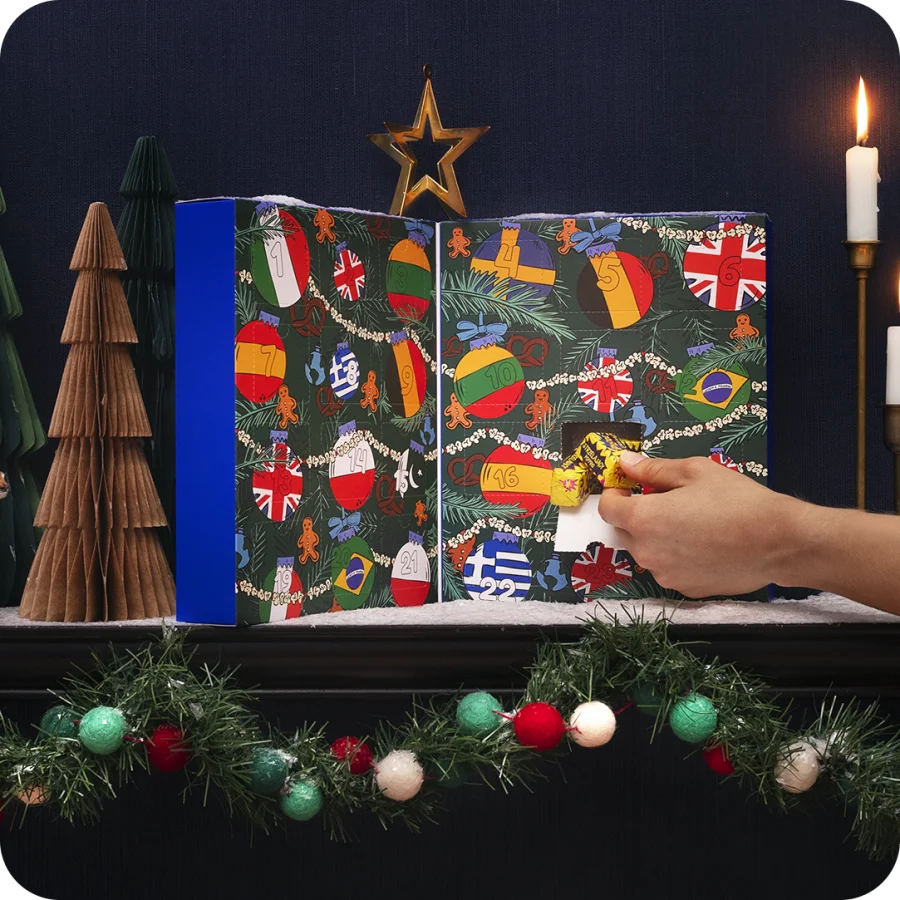 The open Around The World Candy Advent Calendar standing between paper trees and a garland.